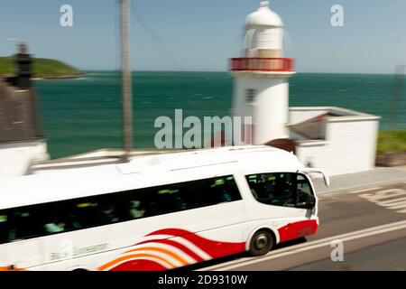 Public transport Ireland. Panning view of Bus Eireann coach passing by the Youghal Lighthouse on sunny day in Youghal County Cork Ireland Stock Photo