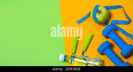 Fitness concept banner with dumbbells, jump ropes and measuring tape on a green and yellow background. Stock Photo