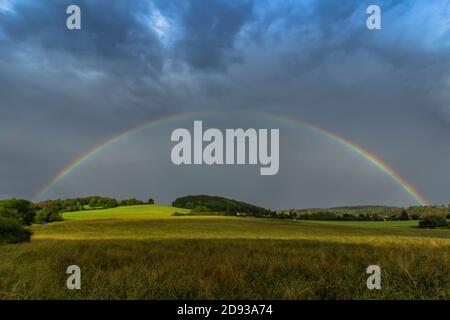 Rainbow and sunbeams illuminate fall meadow.Beautiful intense rainbow colors in rainy day.Weather forecast.Autumn rural landscape with rainbow over da Stock Photo