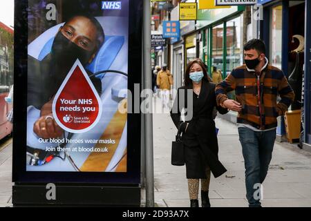 London, UK. 26th Oct, 2020. A couple wearing face masks walks past a 'Your NHS Needs You' sign in London. The publicity campaign board asks members of public to donate blood to NHS Credit: Dinendra Haria/SOPA Images/ZUMA Wire/Alamy Live News Stock Photo