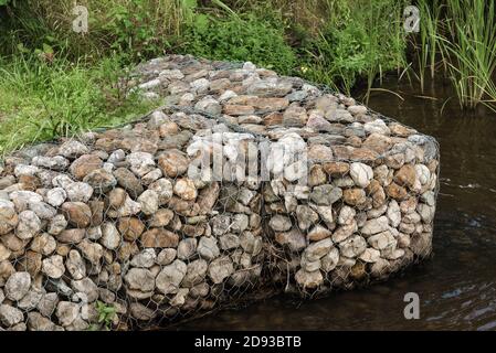 Decorative blocks with pebbles in mesh on calm pond bank Stock Photo