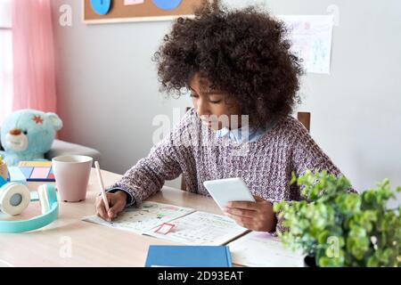 African kid school girl using mobile phone app online learning class at home. Stock Photo