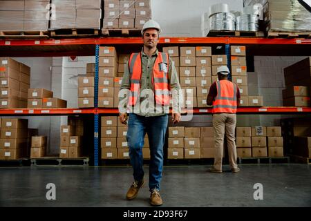 Handsome factory worker wearing overalls walking around warehouse  Stock Photo