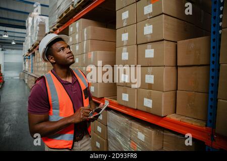 African American male worker searching for delivered packages holding digital tablet in warehouse  Stock Photo