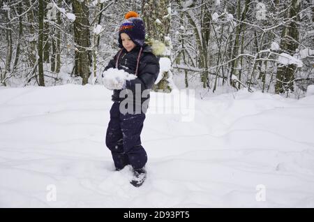 A simpotic little boy throws snow in the winter snow-covered forest, trees in the snow. enjoys the winter. plays snowballs. happy, smiling, laughing Stock Photo