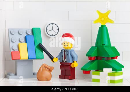 Tambov, Russian Federation - November 2, 2020 Lego minifigure businessman wearing a Santa hat and pointing out company growth on a chart.