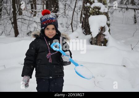 A simpotic little boy throws snow in the winter snow-covered forest, trees in the snow. enjoys the winter. plays snowballs. happy, smiling, laughing Stock Photo