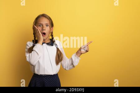 Young student is with shocked expression and indicates something. Yellow background. Stock Photo