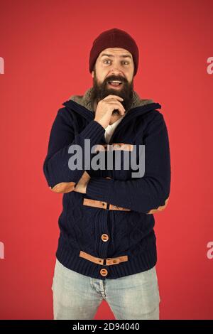 Warm and comfortable. Fashion menswear shop. Masculine clothes concept. Winter menswear. Clothes design. Man bearded warm jumper and hat red background. Winter season menswear. Personal stylist. Stock Photo