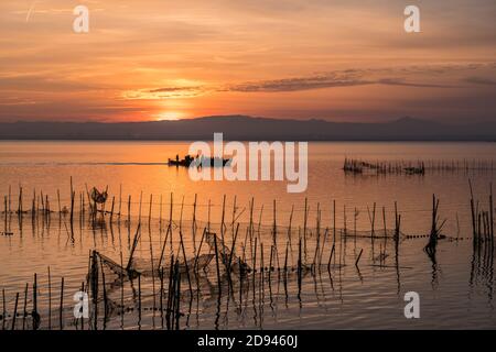 Sunset pier Albufera Valencia tourist ride boat reflections orange sky in the lake Natural ural Park Spain. traditional fishing nets in the water Stock Photo