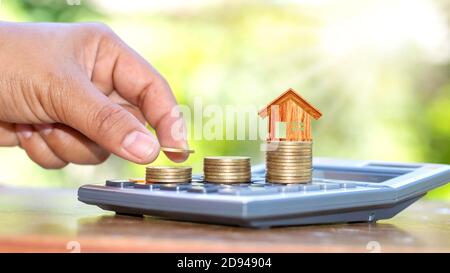 The hand that is holding the coin and free it on the coin stack includes the house model on the coin and a calculator. Stock Photo