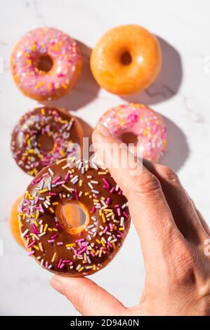 Doughnuts with different glaze, traditional sweet pastries topped with sprinkles on white marble background Stock Photo