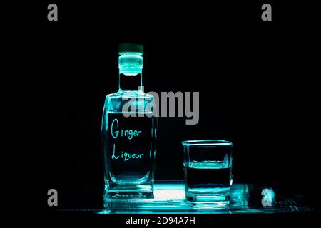 Bottle of Ginger Liqueur and Shot Glass on Black Background with Blue Light Stock Photo