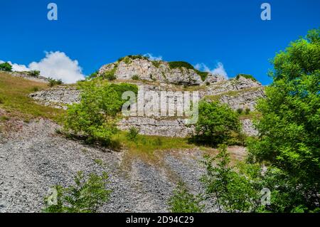 Spectacular limestone outcrop, with prominent bedding planes and loose scree slopes, high above the River Lathkill in Derbyshire on a summer day. Stock Photo