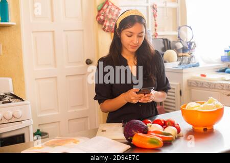 Beautiful Hispanic woman cooking while using tablet computer in kitchen ...