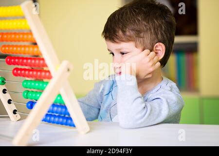 Caucasian toddler boy feeling bored and tired while playing with abacus at kindergarten Stock Photo