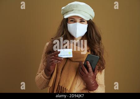 Life during coronavirus pandemic. happy young female in sweater with smartphone, white medical mask and credit card making online purchases on e-comme Stock Photo