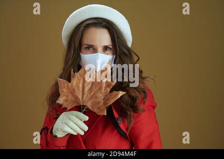 Hello autumn. Portrait of trendy middle aged housewife in red coat with yellow autumn maple leaf on brown background. Stock Photo