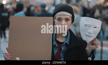 Young woman removing Theater mask while holding black cardboard in the crowd. Protest against discrimination. High quality photo Stock Photo