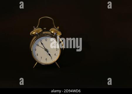 Closeup of a gold alarm clock against a  black background Stock Photo