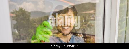 A young man cleaning the window with a window cleaner BANNER, LONG FORMAT Stock Photo