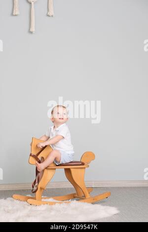 Child Sitting On Ride On Toy In Playroom. Toddler Baby Boy Riding Swinging On Rocking Chair Toy Horse Stock Photo