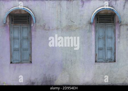 old house building with two wooden windows and a broken wall. old house in rural indonesia. mossy wall texture for the background Stock Photo