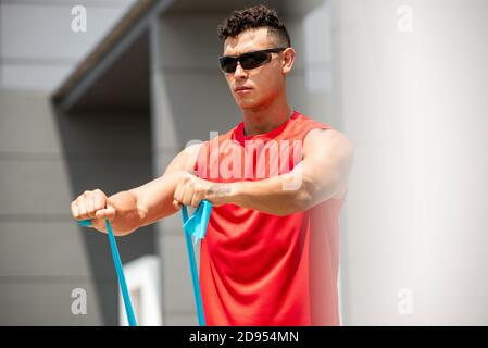 Handsome sports man doing shoulder front raise morning exercise with resistance band outdoors Stock Photo