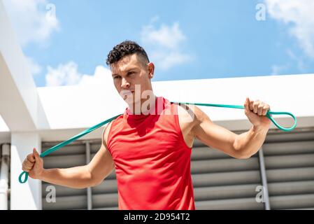 Handsome athletic man stretching with resistance band outdoors on building rooftop, home exercise concept Stock Photo