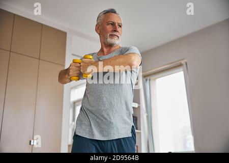 Enthusiastic elderly man working out with dumbbells at home Stock Photo