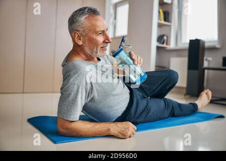 Active pensioner staying hydrated while exercising at home Stock Photo