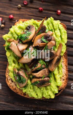 Avocado toast with fried mushrooms on a wooden background. Top view. Healthy vegan avocado toast Stock Photo