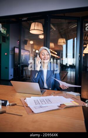 Cheerful female architect having phone conversation at work Stock Photo