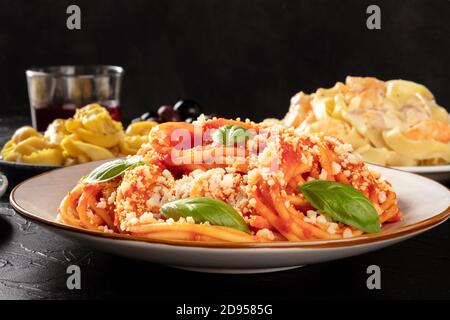 Pasta with tomato sauce, basil and Parmesan, a close-up in a restaurant with other blurred food and wine in the dark background, selective focus Stock Photo