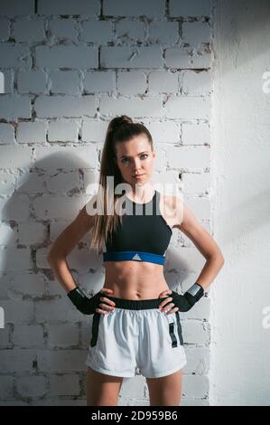 A pretty long-haired brunette of athletic build stands against a brick wall in the loft Stock Photo