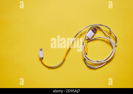An old torn USB cord is lying on a yellow background. The view from the top. layout Stock Photo