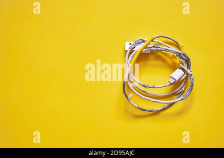 An old torn USB cord is lying on a yellow background. The view from the top. layout Stock Photo