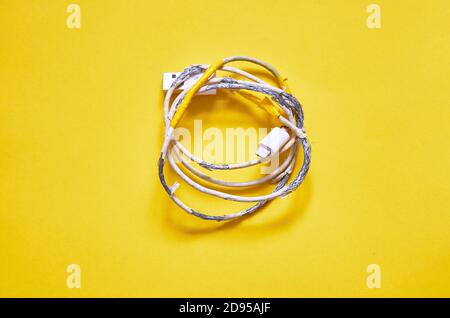 An old torn USB cord is lying on a yellow background. The view from the top. layout Stock Photo