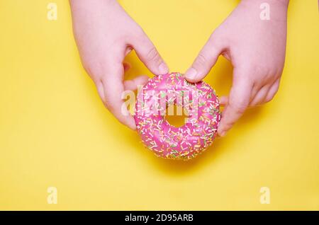 Two hands hold a pink donut. The view from the top. Yellow background. Stock Photo