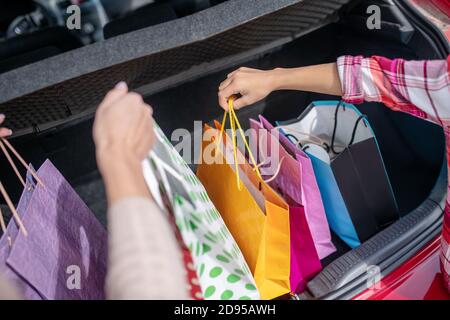 Close-up of two pairs of hands taking out shopping bags from car boot Stock Photo
