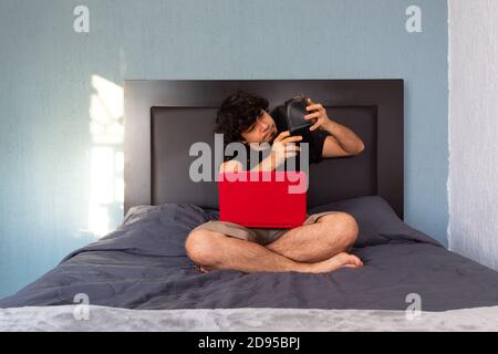 Hispanic young man sitting on a bed looking at his wallet with no money Stock Photo