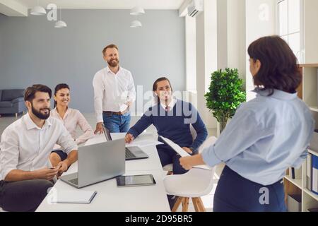 Woman making report for team of positive company colleagues in corporate meeting Stock Photo