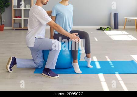 Young woman doing back fitness exercise on fitball with physiotherapist or chiropractor helping her Stock Photo