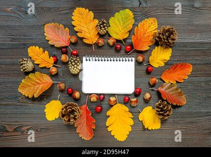 Autumn frame with fallen leaves and empty white notepad on the wooden background Stock Photo