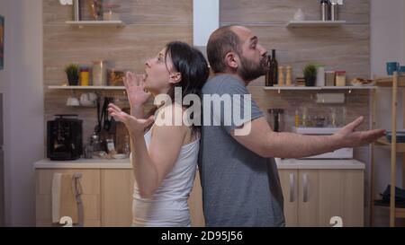 Angry people arguing standing back to back. Furious, irritated, frustrated, jealous unhappy couple screaming accusing to each other having family conflict disputing sitting in the kitchen. Stock Photo