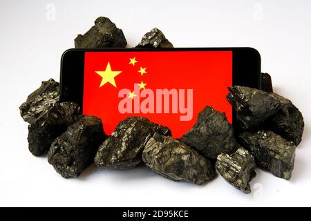 China’s coal addiction. Concept. Chinese industry and technology rely on coal and coal mining. Flag of China seen on the smartphone surrounded by coal Stock Photo