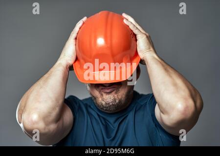 Extremely stressed engineer in hardhat against gray background Stock Photo