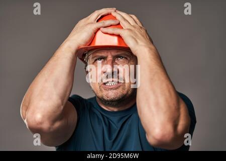 Extremely stressed engineer in hardhat against gray background Stock Photo