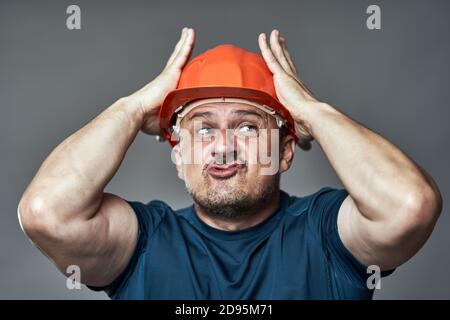 Extremely stressed engineer in hardhat against gray background Stock Photo