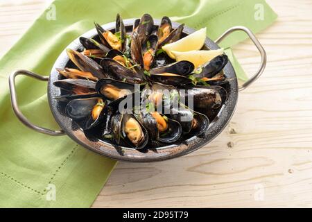 Mussels with lemon and parsley served in a bowl, green napkin and bright wooden table with copy space, selected focus, very narrow depth of field Stock Photo